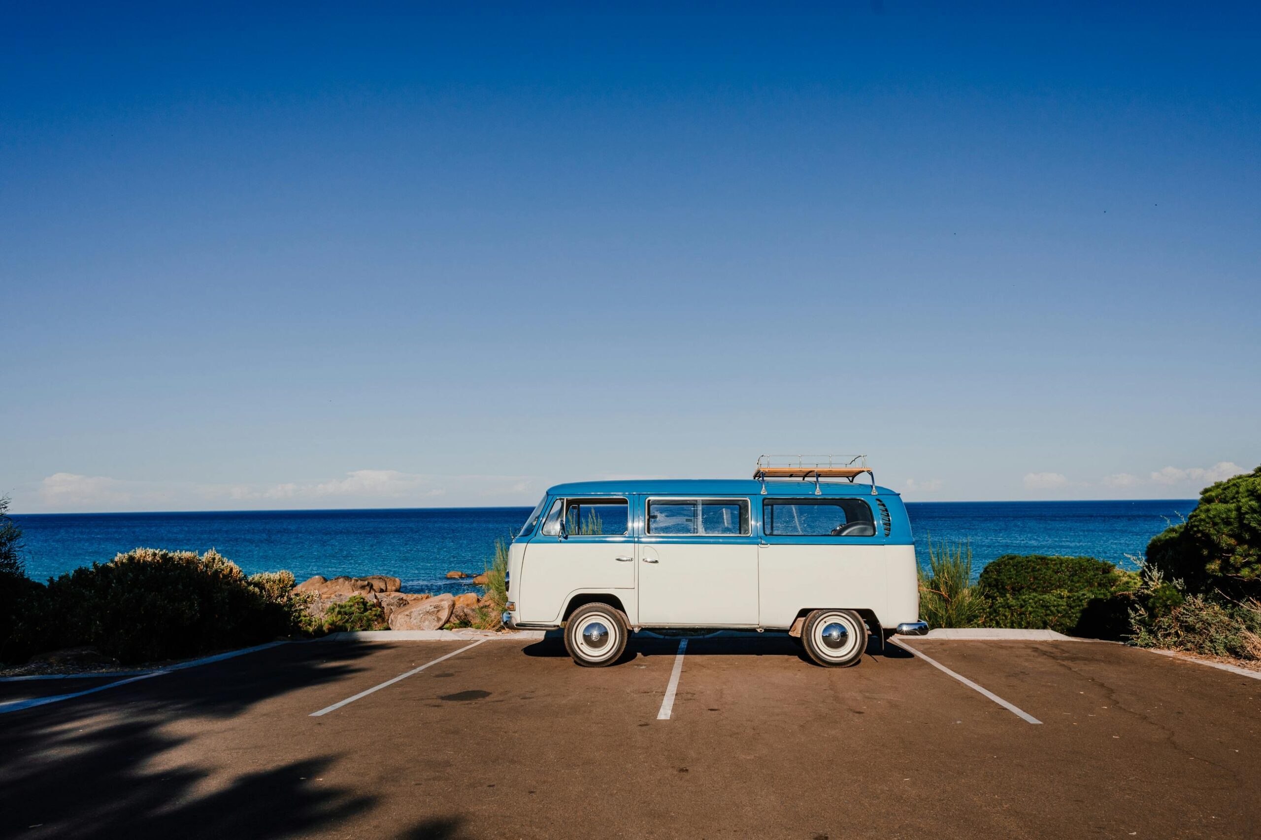 Vibrant blue cloudless sky over vintage trailer parked on asphalt next to coast blue endless ocean in sunlight