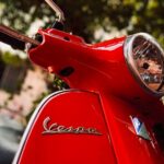 Vibrant red Vespa scooter headlight and emblem in focus, showcasing classic Italian design.