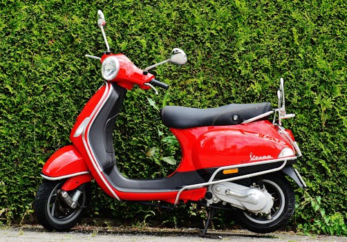 Bright red Vespa scooter parked against a lush green hedge showcasing vibrant contrast