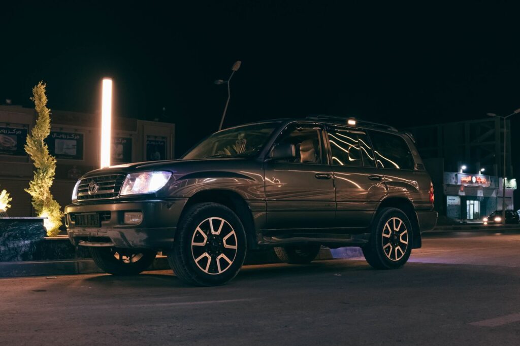 A dark SUV parked under streetlights on a city street at night, showcasing urban aesthetics.